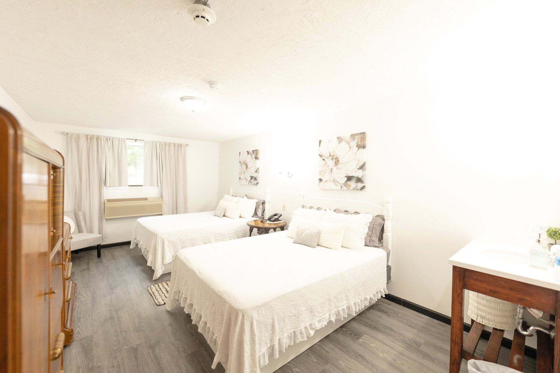 Bright bedroom with two queen beds, white bedding, and a wooden dresser.