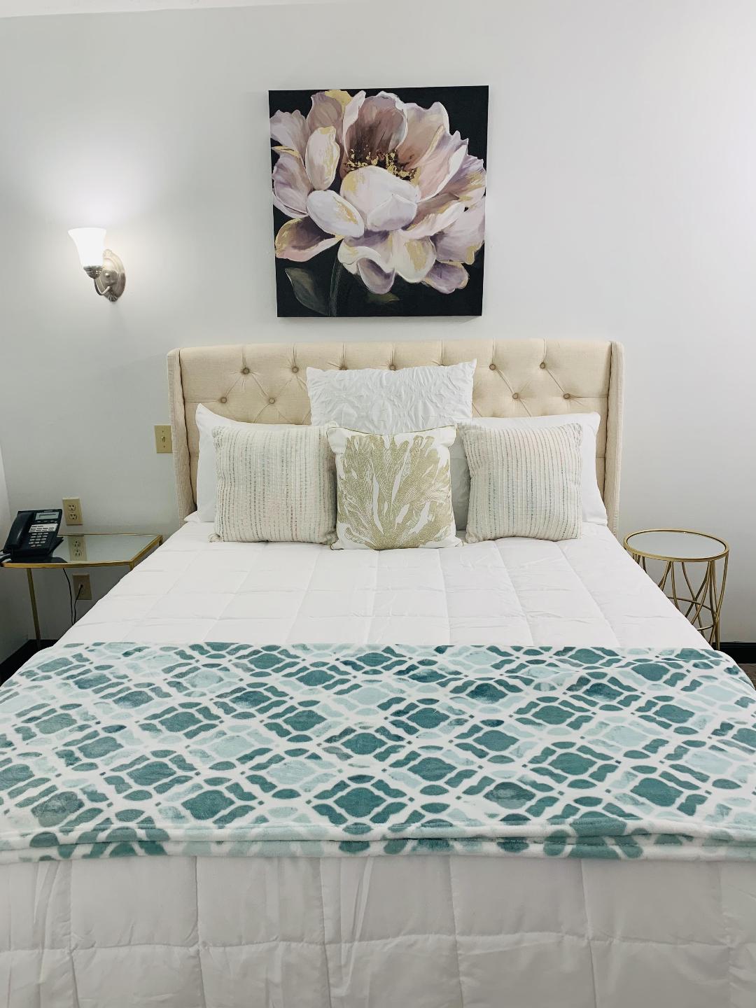 Bedroom with bed, floral art, accent pillows, patterned teal throw, and bedside tables.