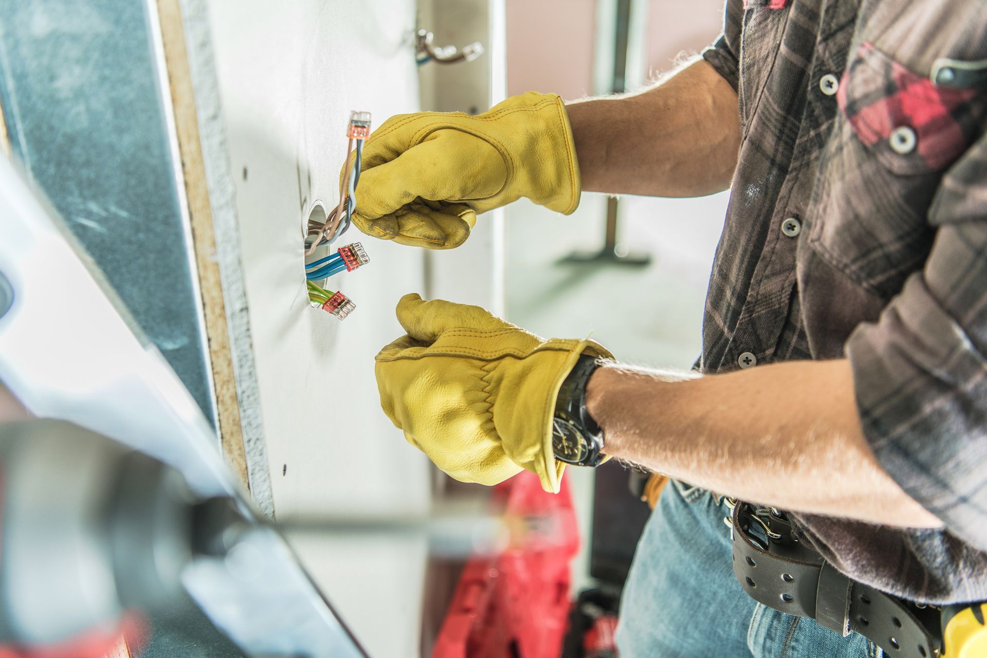 Male residential electrician with a safety hat and yellow gloves installs an outlet on a building’s wall. Male residential electrician with a safety hat and yellow gloves installs an outlet on a building’s wall.