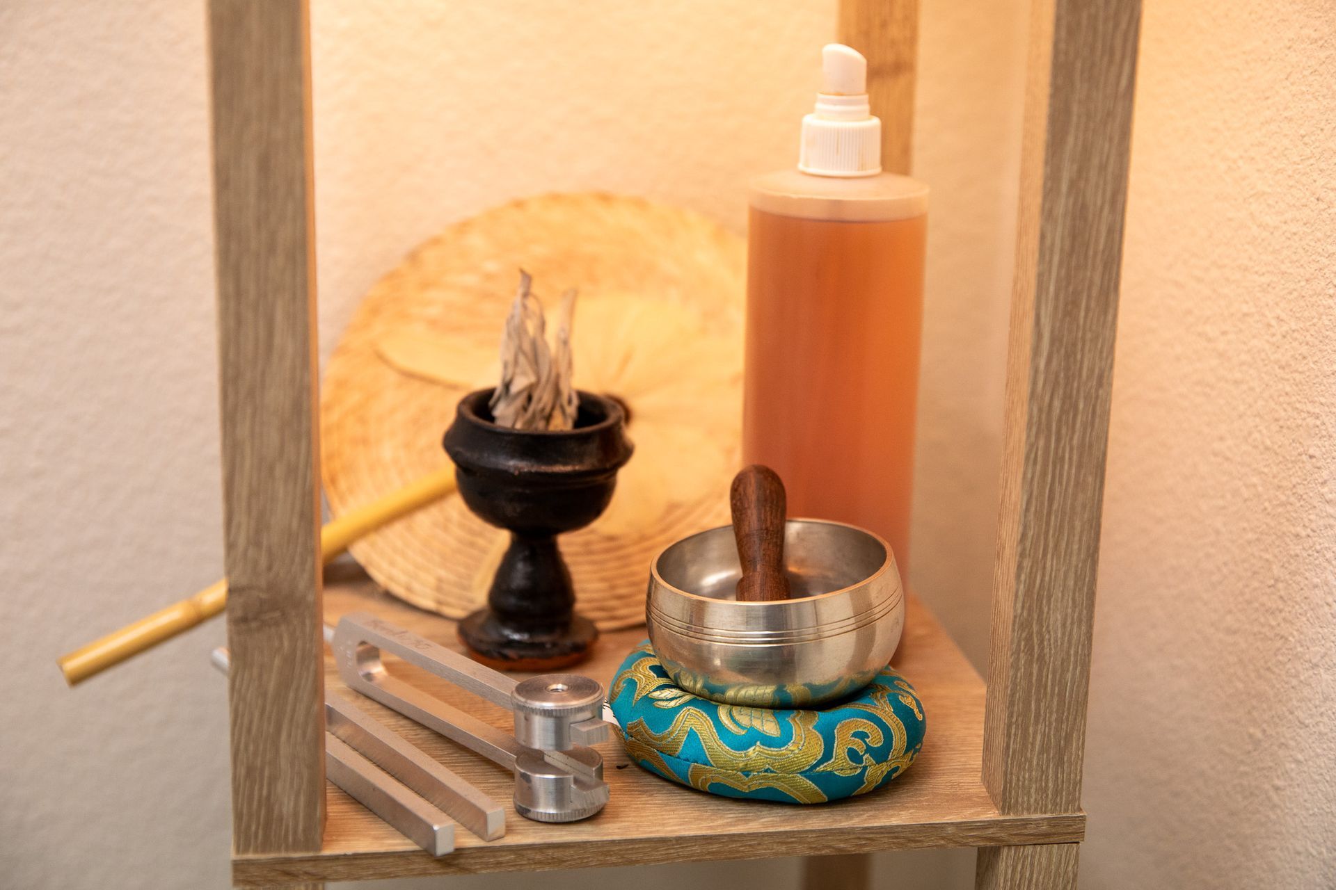 Small shelf with a bowl, incense burner, wooden stick, and an amber bottle against a warm wall.
