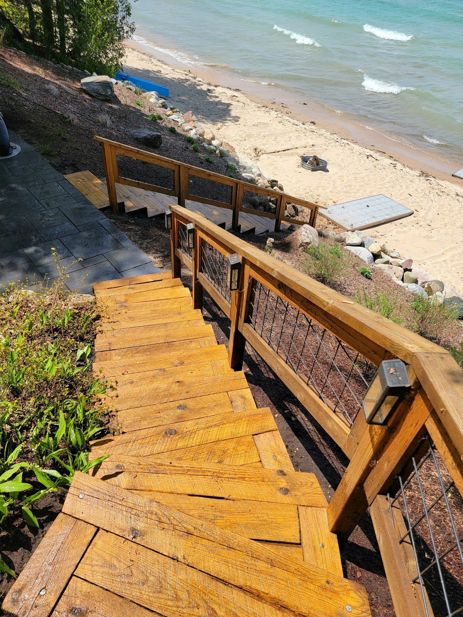 Wooden stairs lead down a sandy beach. The stairs have a wooden railing with metal mesh.