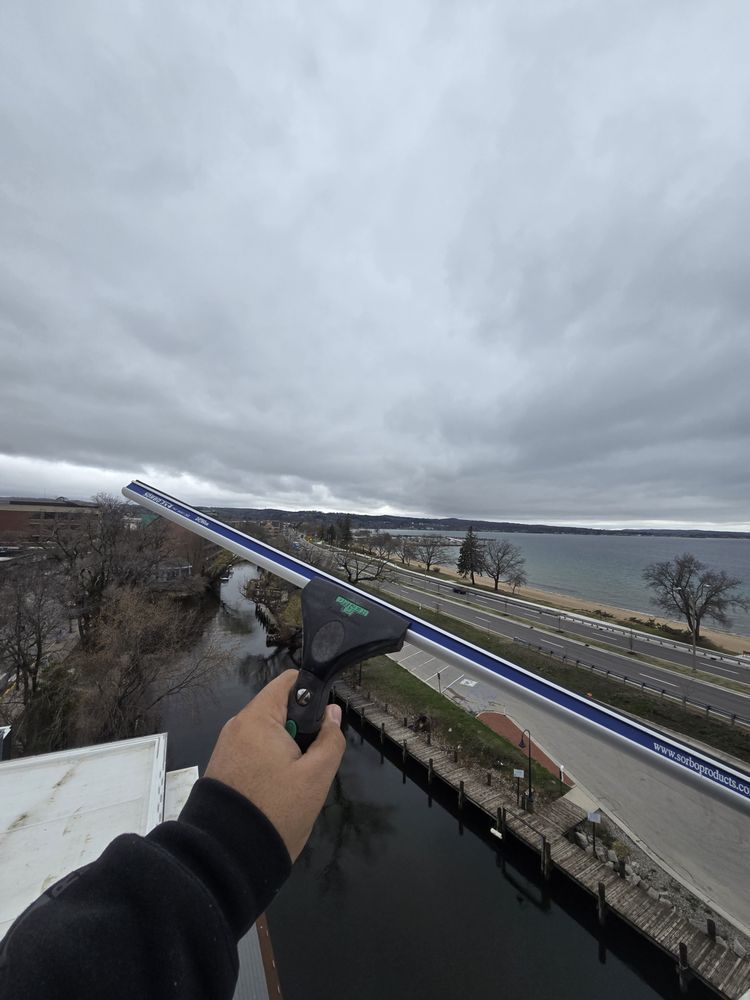 A person holding a window squeegee, cleaning a window with a view of a road, water, and overcast sky.