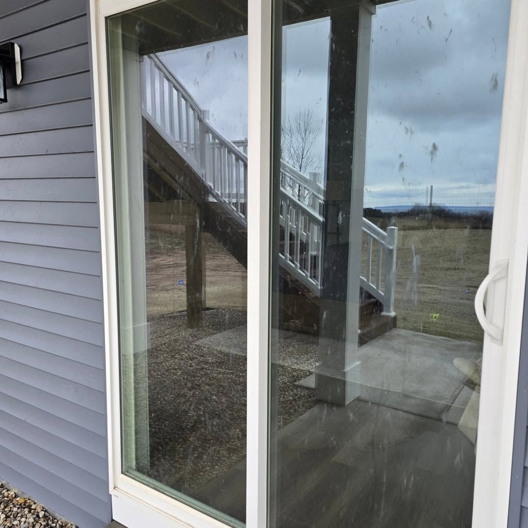 Sliding glass door reflecting a deck with white railing and a cloudy sky.