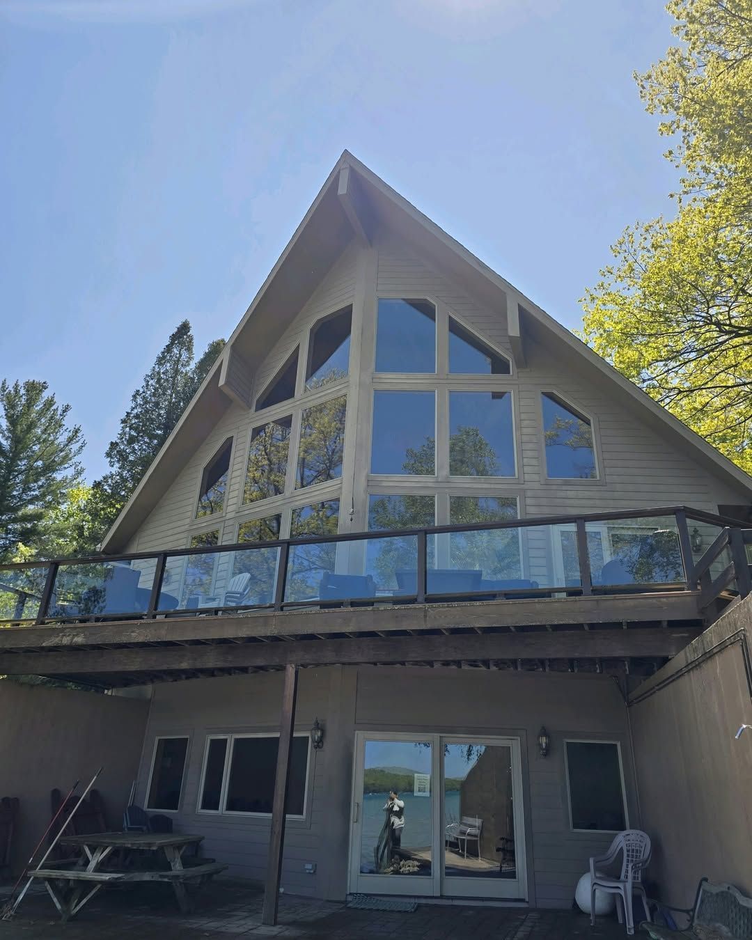 A-frame house with large windows and a glass-railed deck overlooking a lake. The building has a tan exterior.