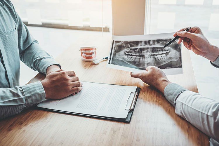 Dentist pointing to dental X-ray while consulting with a patient in an office setting.
