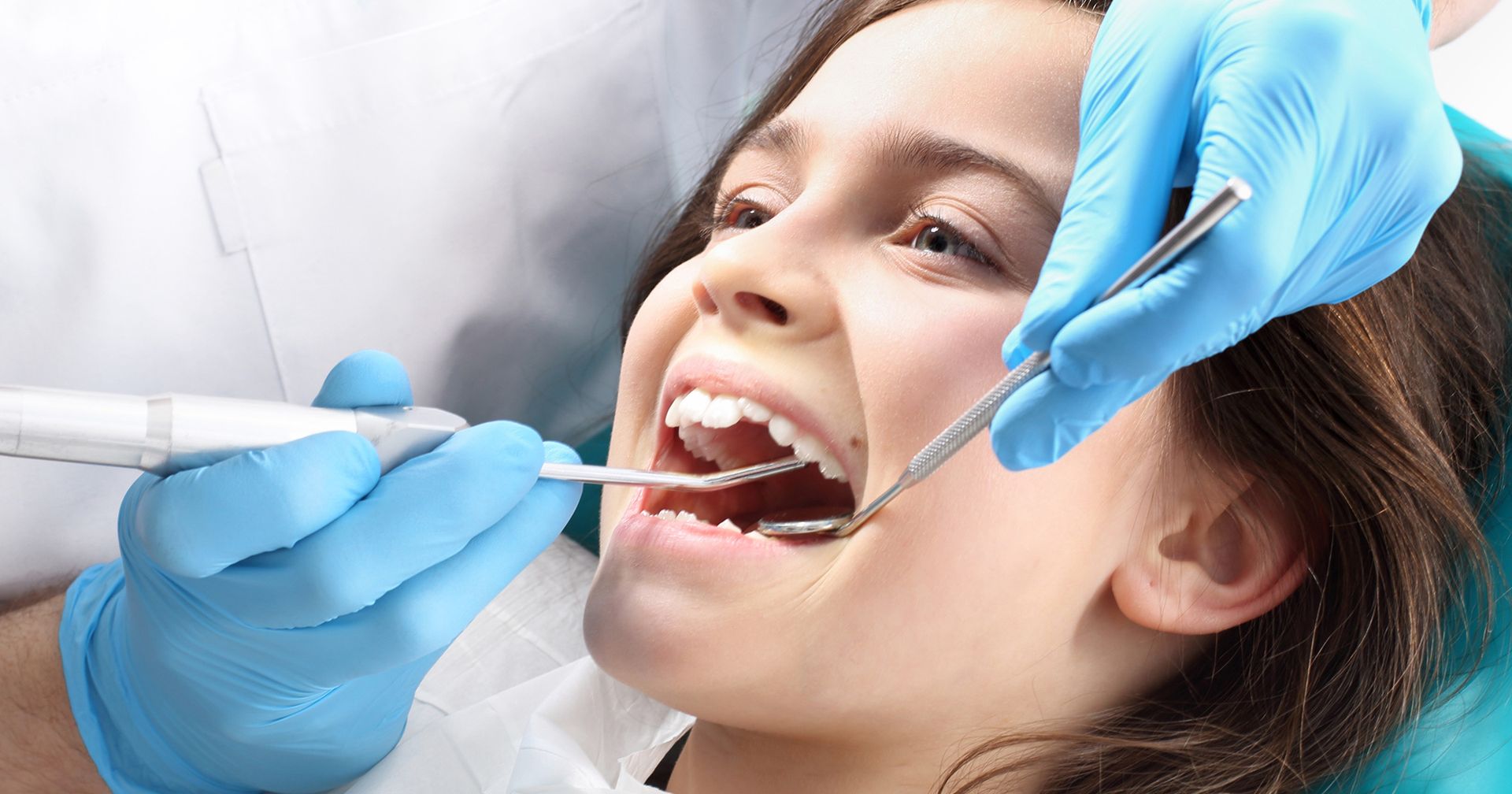 Dentist examining a patient's open mouth with dental tools and blue-gloved hands