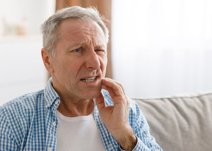 Man holding jaw, grimacing in pain, indoors.