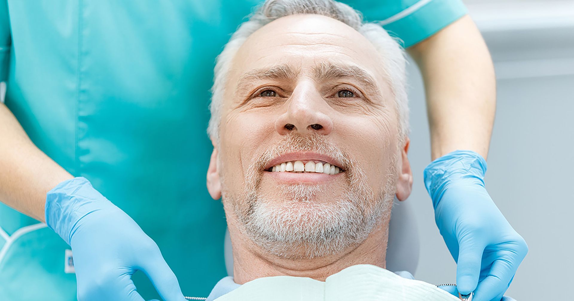 Dentist’s gloved hands working in a patient’s mouth, with the patient smiling in a dental chair.