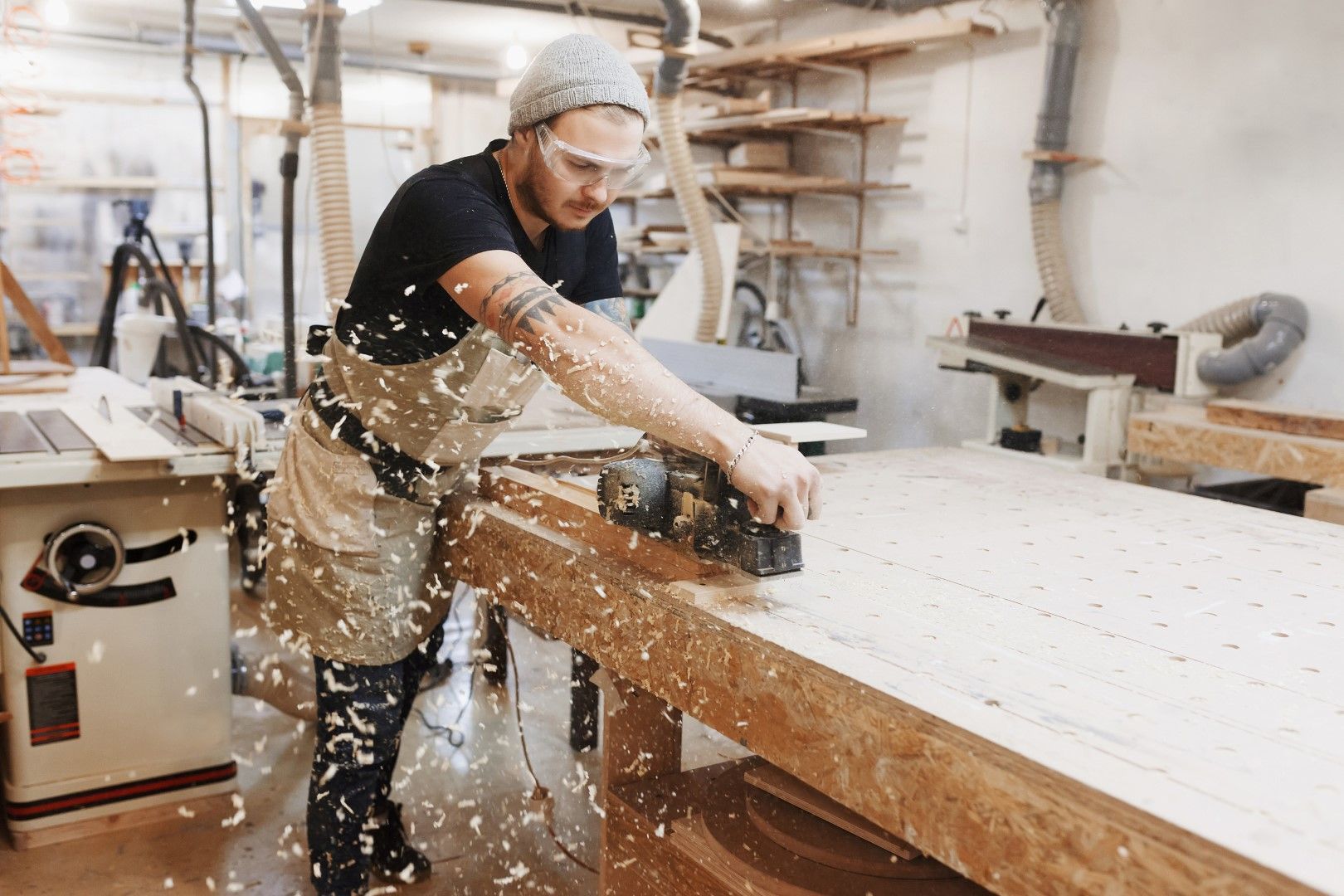 Woodworker using a power planer on a wooden surface, covered in wood shavings.