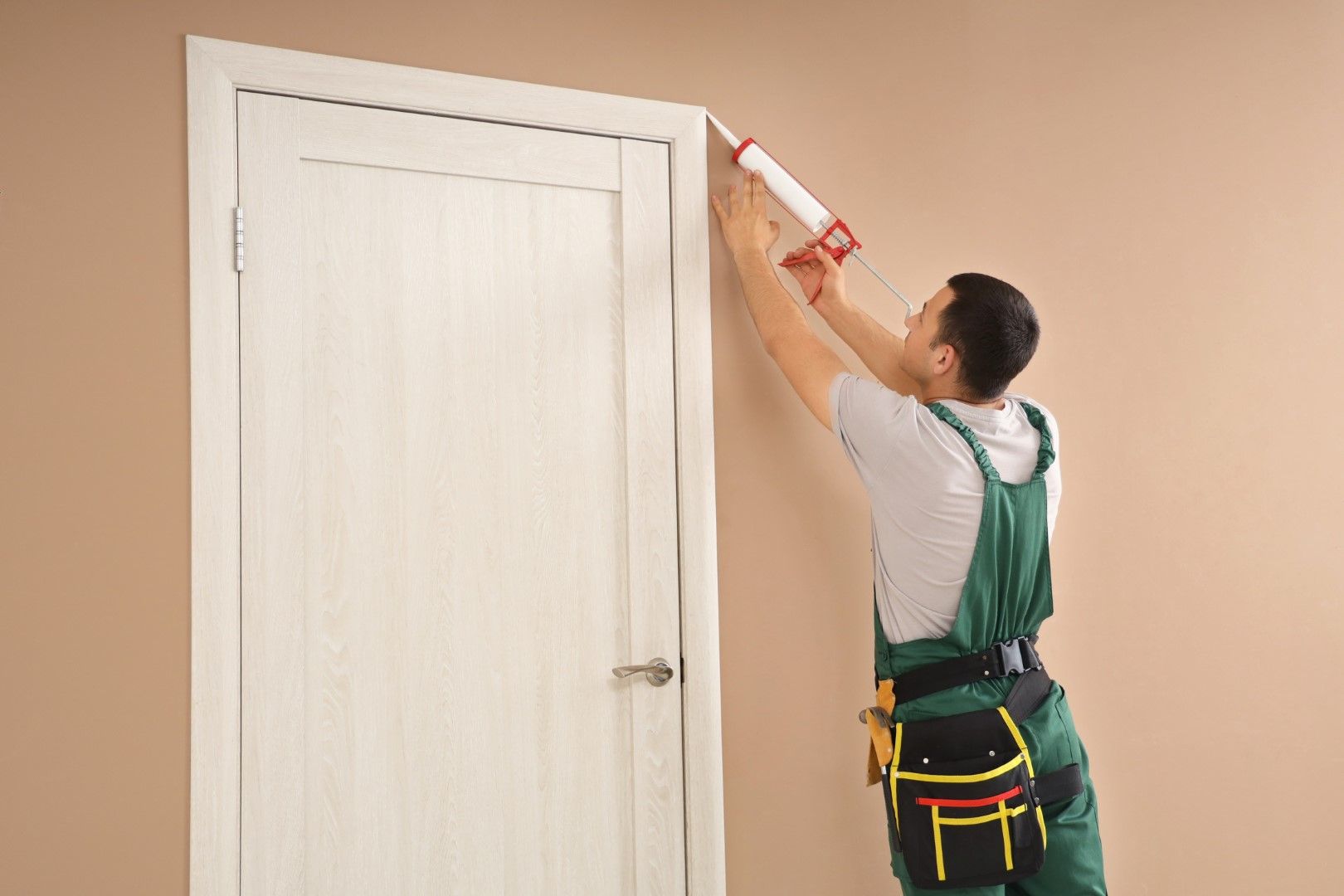 Person sealing door frame with caulk gun.