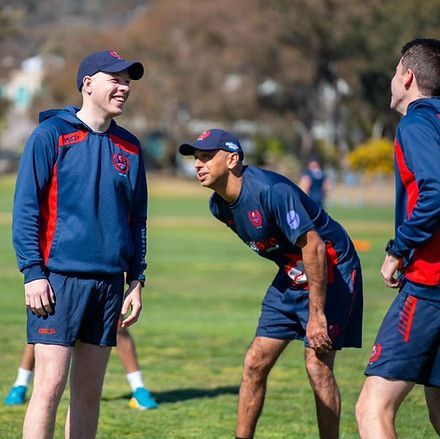 Three soccer players in navy and red training gear laughing on a grassy field