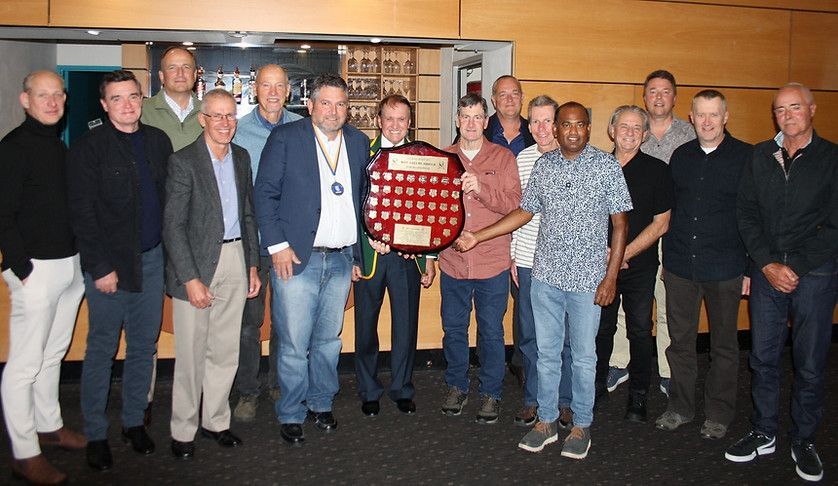 Group of people standing indoors at an awards ceremony, posing with a red plaque in front of a wooden wall.