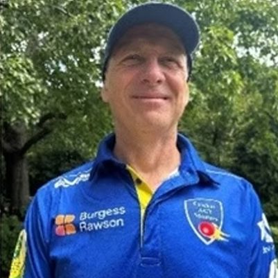 Man in a blue cap and blue team jersey standing outdoors, smiling at the camera.
