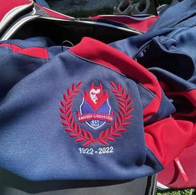 Blue and red sports jersey with a wolf crest and “1922–2022” emblem on fabric pile