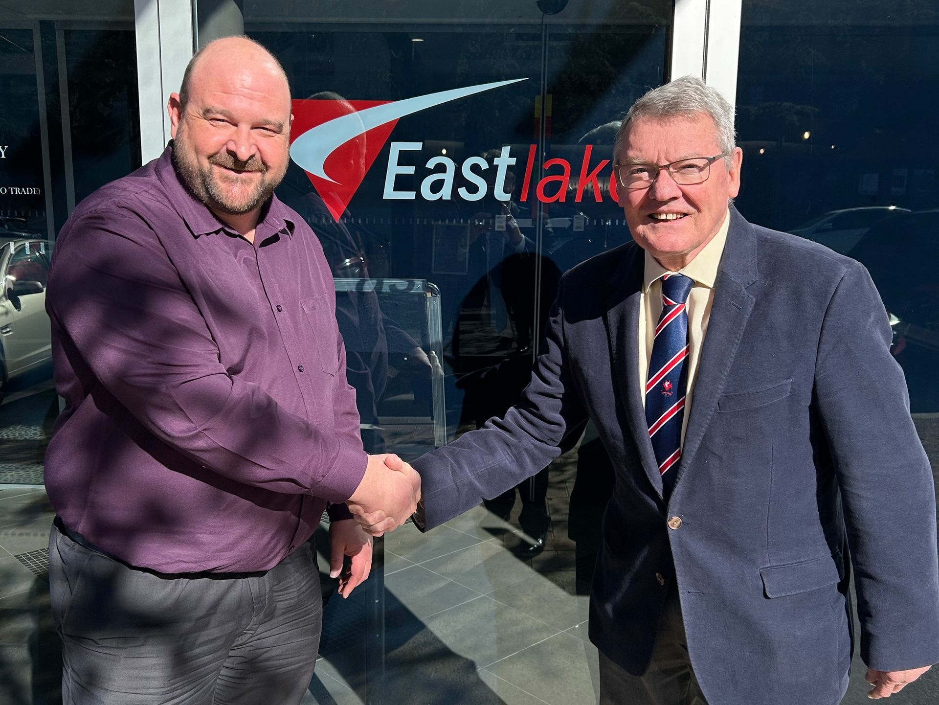 Two men shake hands outside an Eastlake office, one in a purple shirt and one in a blue suit.