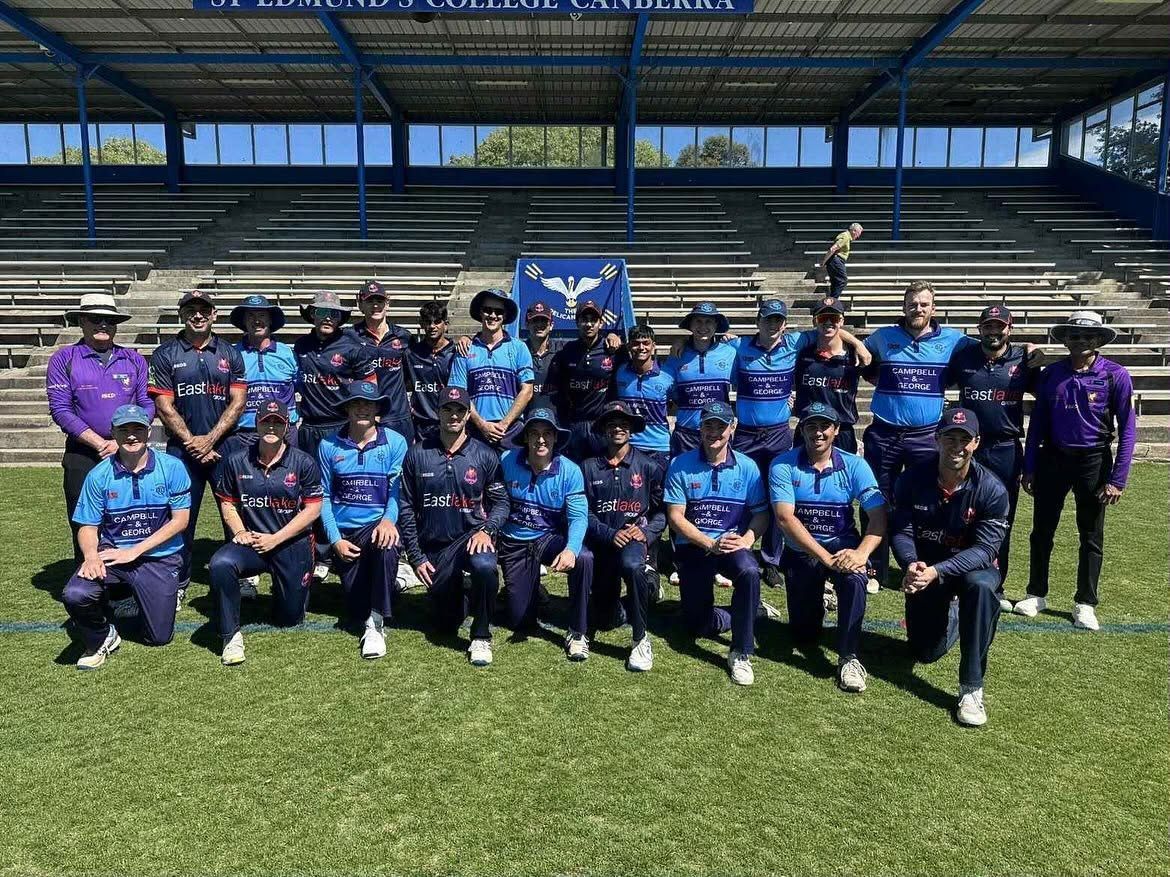 Sports team posing for a group photo on a field, wearing blue and purple jerseys in a stadium