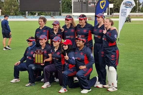 Cricket team in navy and red uniforms posing with a trophy on a field