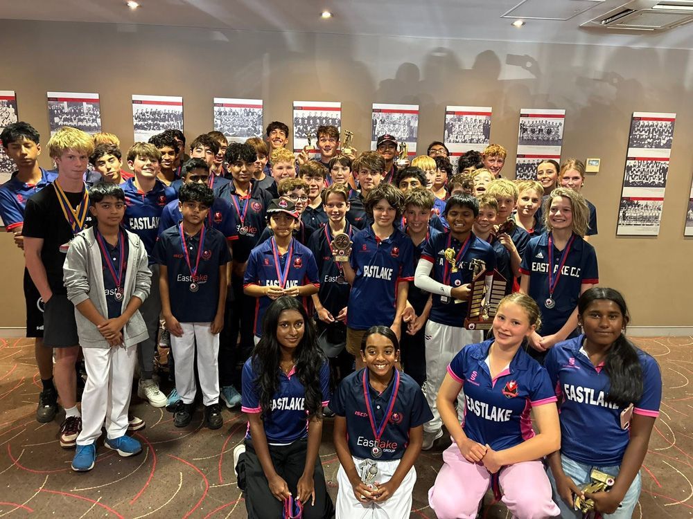 Group of students in blue sports jerseys posing indoors with medals, trophies, and championship banners behind them