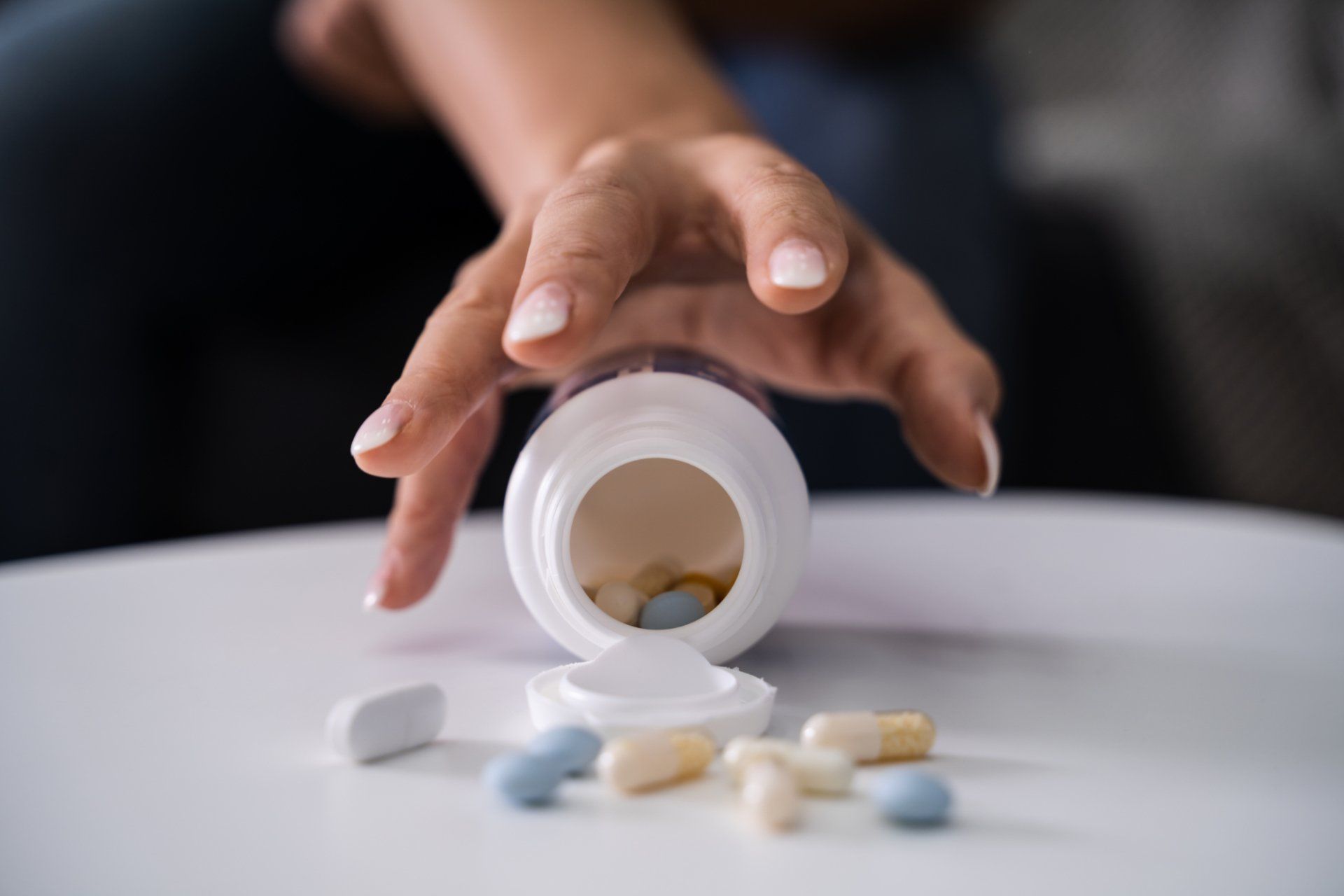 A woman is pouring pills out of a bottle on a table.