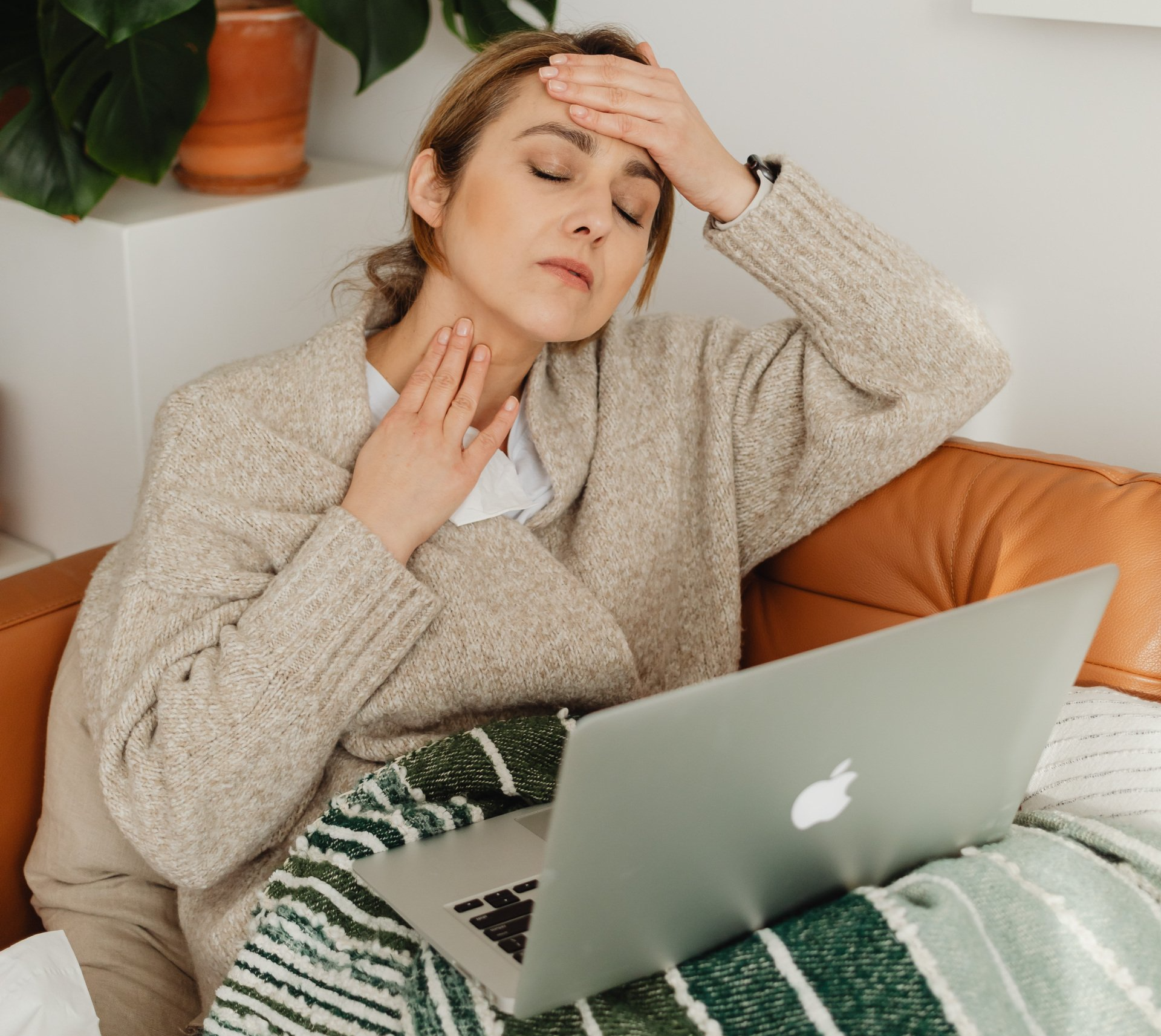 A woman is sitting on a couch with a laptop and holding her head.