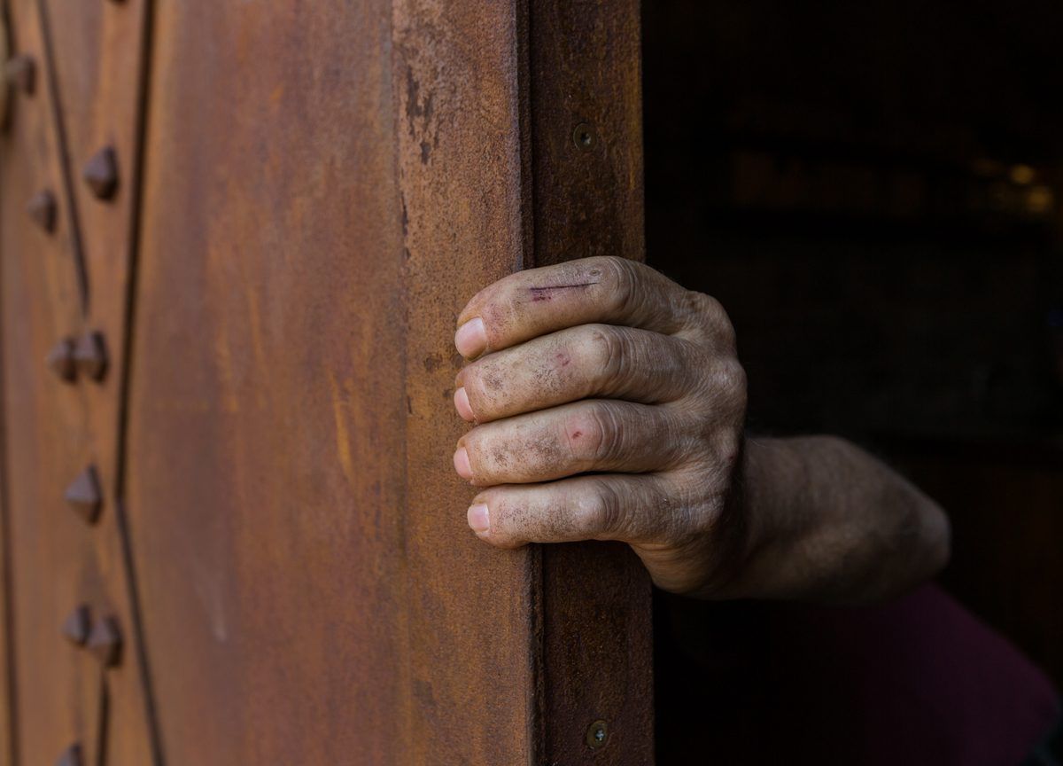 Hand opening a weathered wooden door with iron hardware.