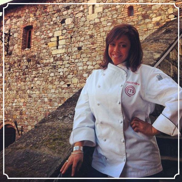 Woman in chef's coat, standing in front of a stone building with a confident expression.