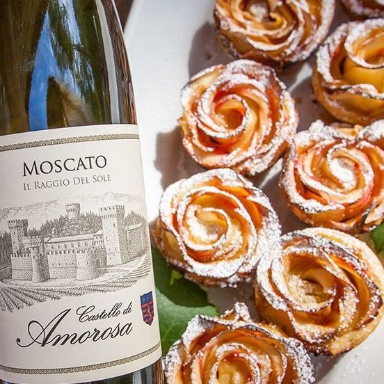 Moscato wine bottle beside a plate of apple rose pastries dusted with powdered sugar.