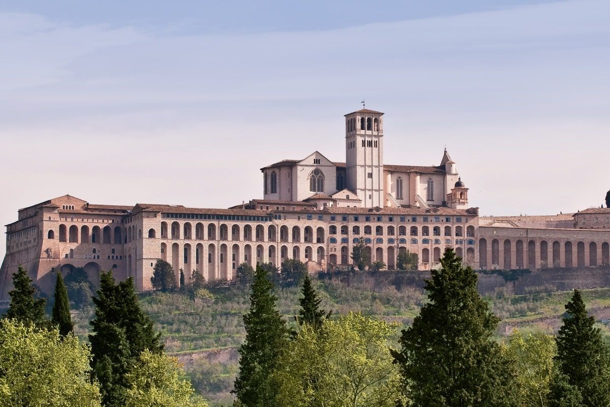Basilica of Saint Francis of Assisi, Italy, seen atop a hill with cypress trees in the foreground.