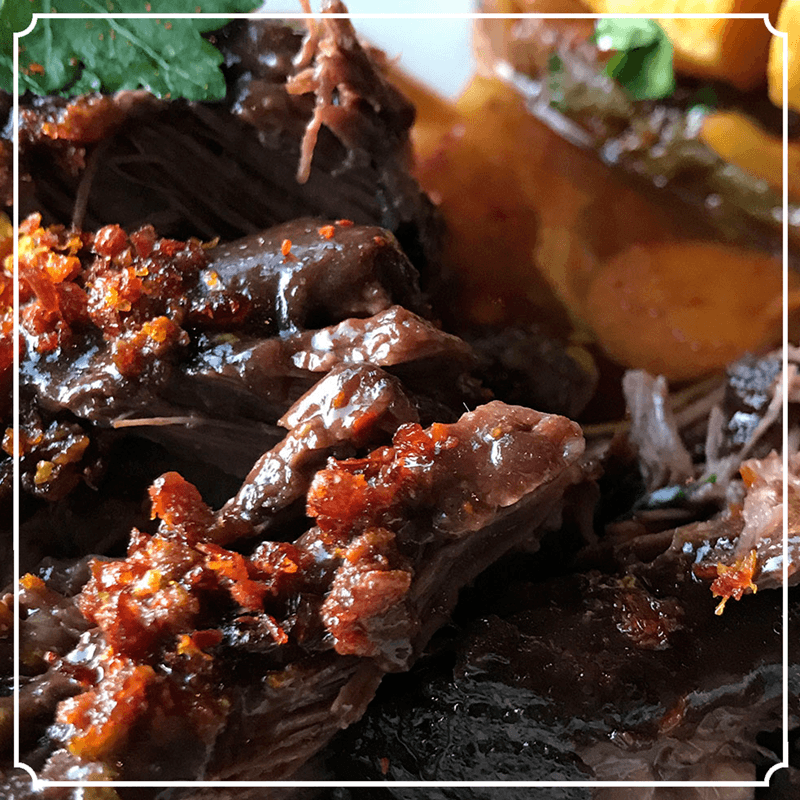 Close-up of braised beef with sauce, and a topping of golden fried onion.