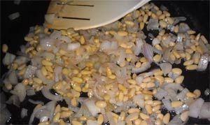 Onions and pine nuts being sauteed in a pan with a spatula.