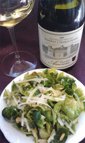 Brussels sprouts salad, wine glass, and bottle of Chardonnay on a table.