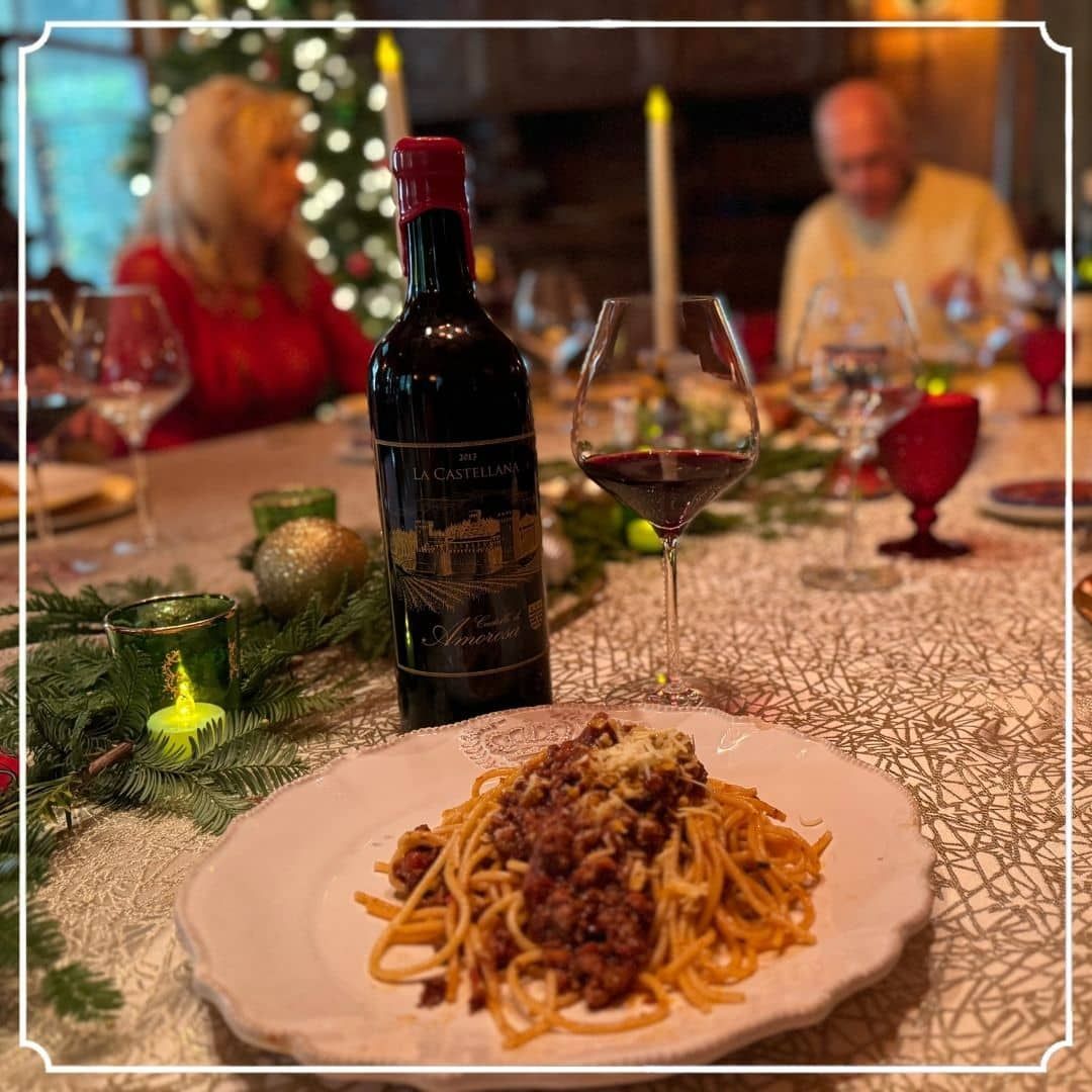 Table setting with spaghetti bolognese, wine bottle, and couple in the background. Christmas holiday scene.
