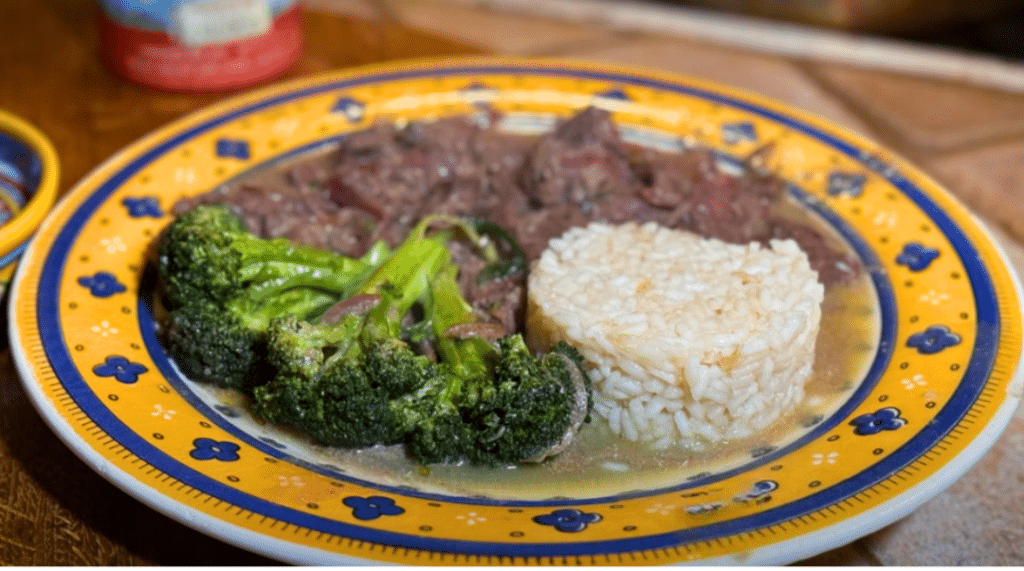 Beef and broccoli dish with a side of rice on a yellow plate.