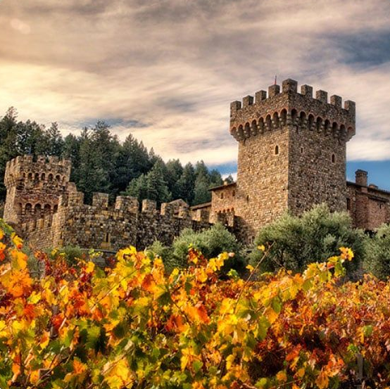 Stone castle with towers amid colorful fall vineyards.