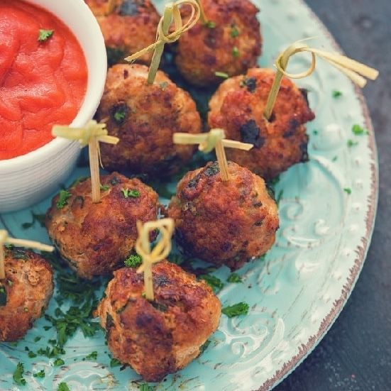 Meatballs with toothpicks on a blue plate, served with red dipping sauce.