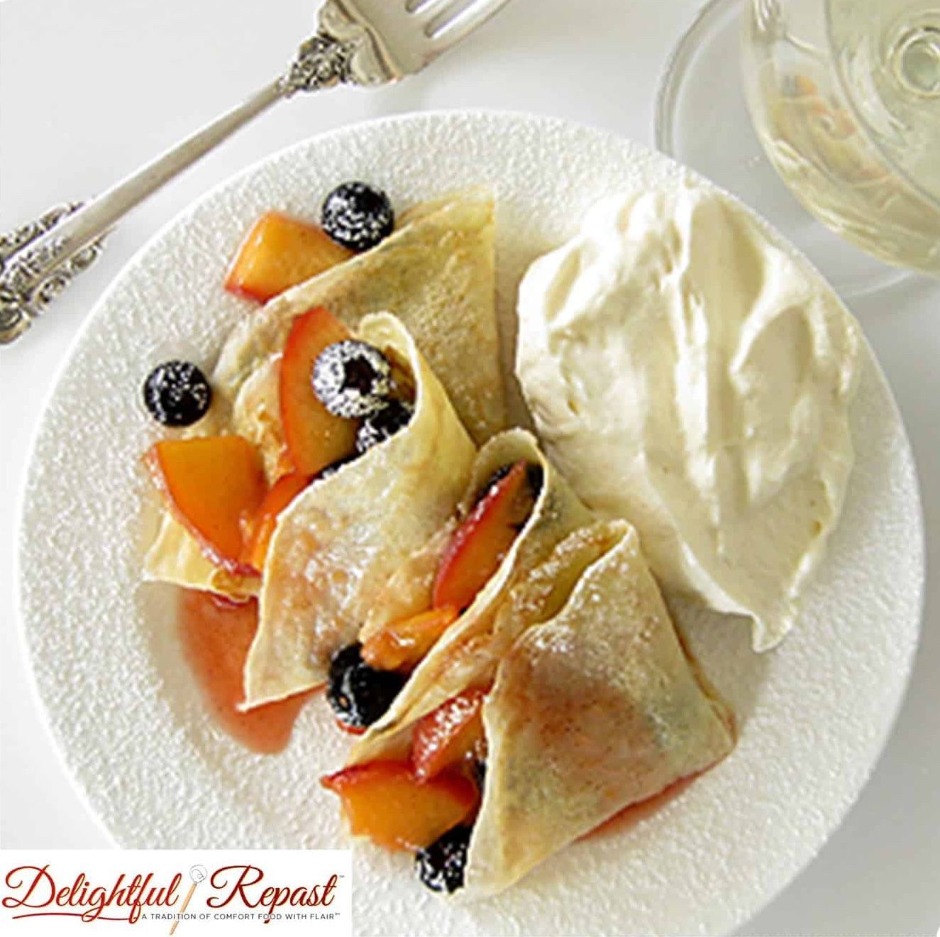 Crepes with peaches, blueberries, and whipped cream on a white plate.