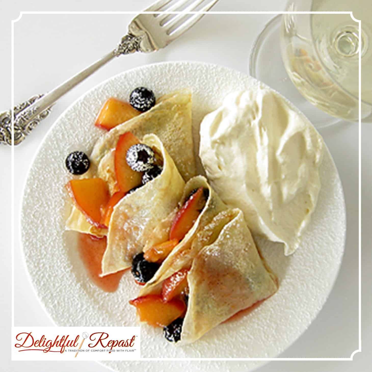 Crepes with peaches, blueberries, and whipped cream on a white plate, served with wine and a fork.