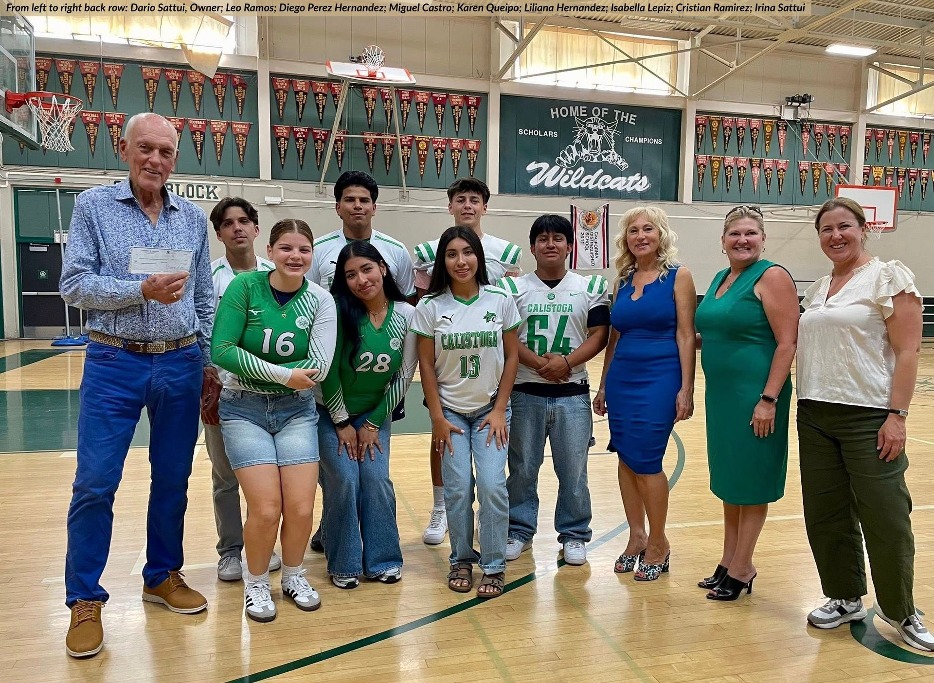 Group of people posing in a gymnasium. Some wearing green and white athletic uniforms, some smiling, banners in the background.