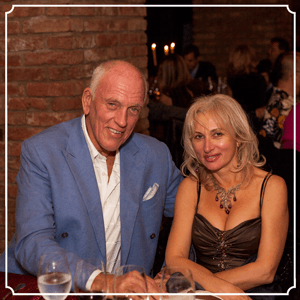 Man in blue jacket and woman in brown dress smiling at table.