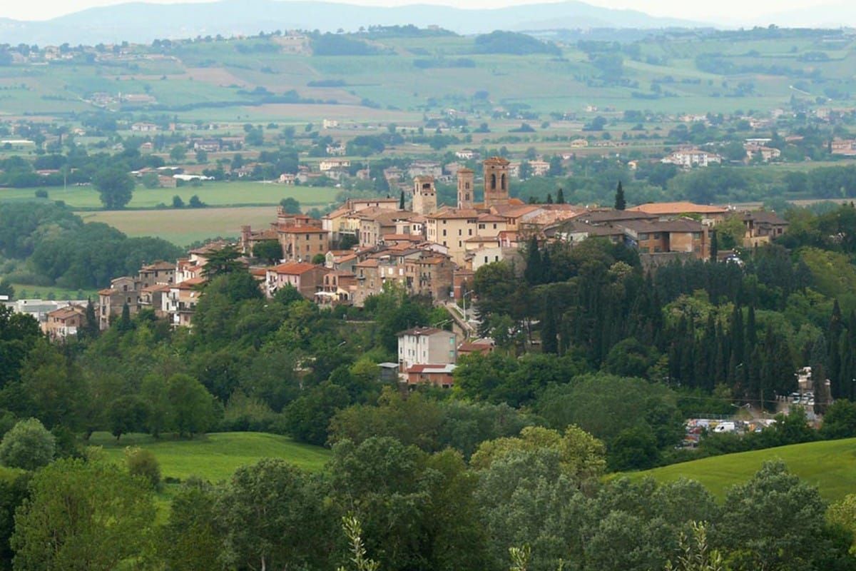 A hilltop town in Italy with stone buildings, two prominent bell towers, and surrounding green hills.
