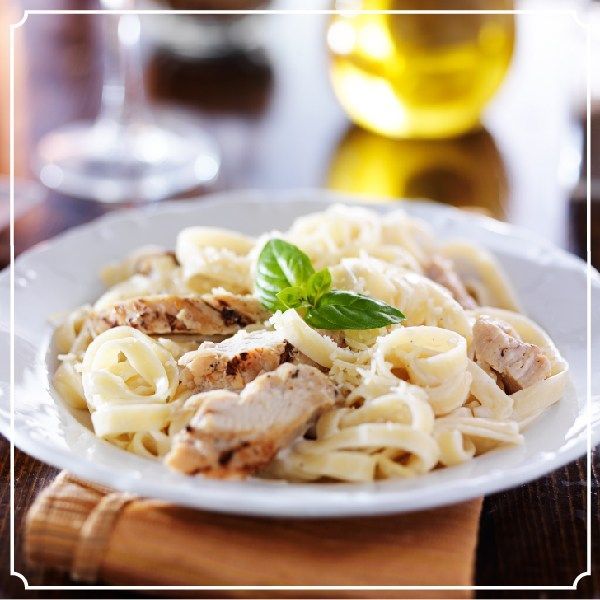 Fettuccine Alfredo with grilled chicken and basil garnish on a white plate.