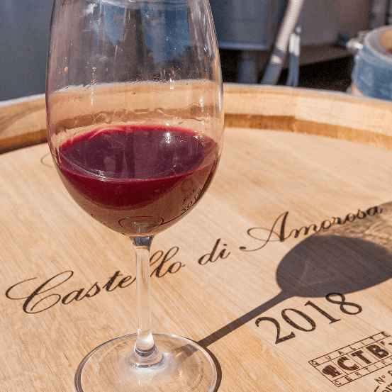 A glass of red wine sits on a wooden barrel with the text 