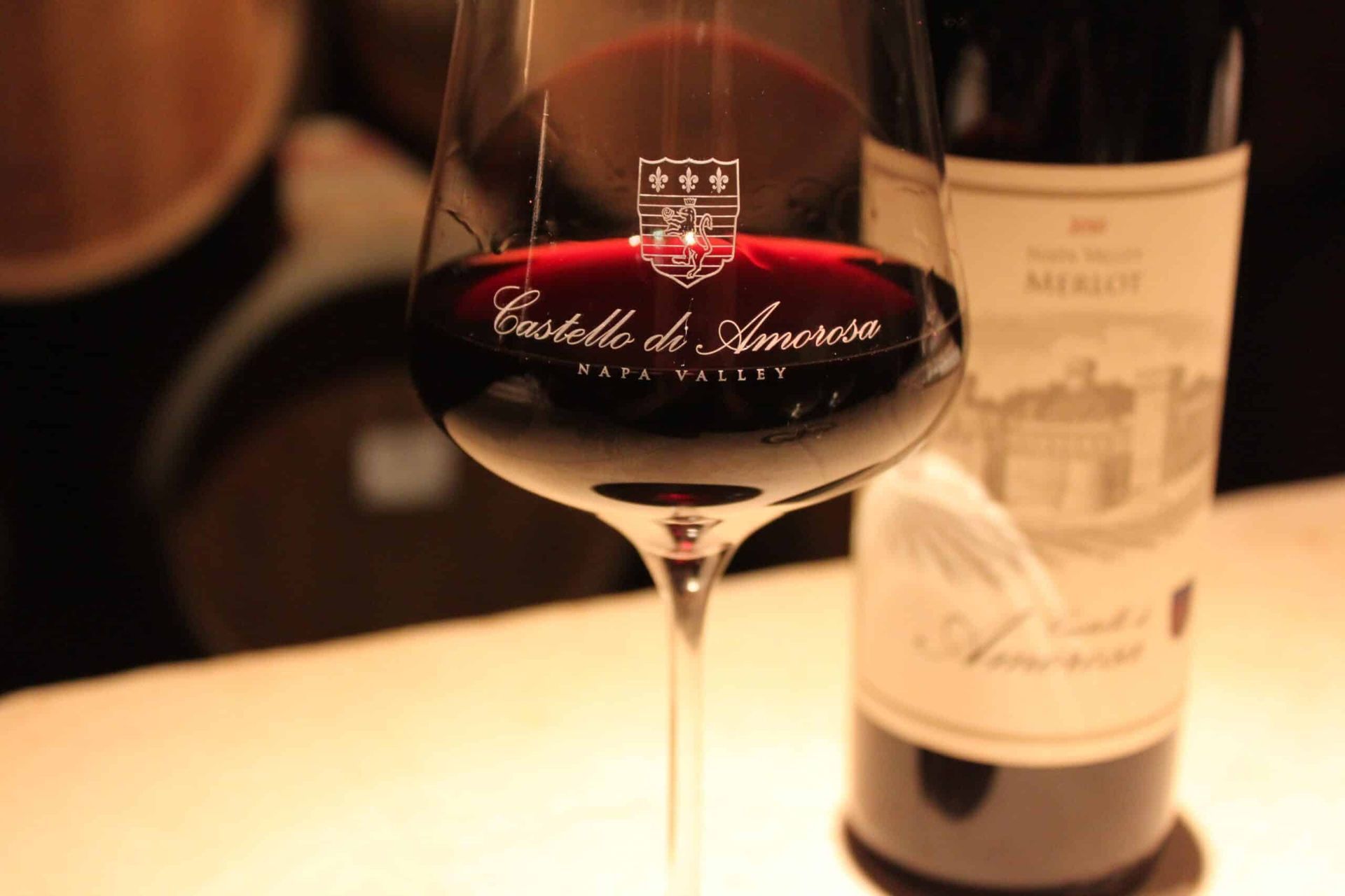Wine glass with red wine and bottle of Castello di Amorosa wine