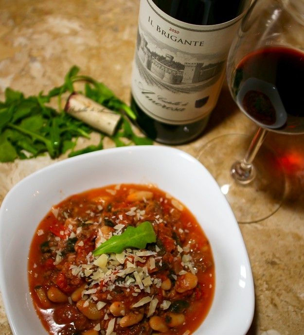 Bowl of white bean soup with wine and greens on a kitchen counter