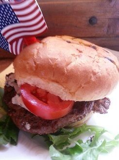 Hamburger with tomato slice, lettuce, and American flag on top.