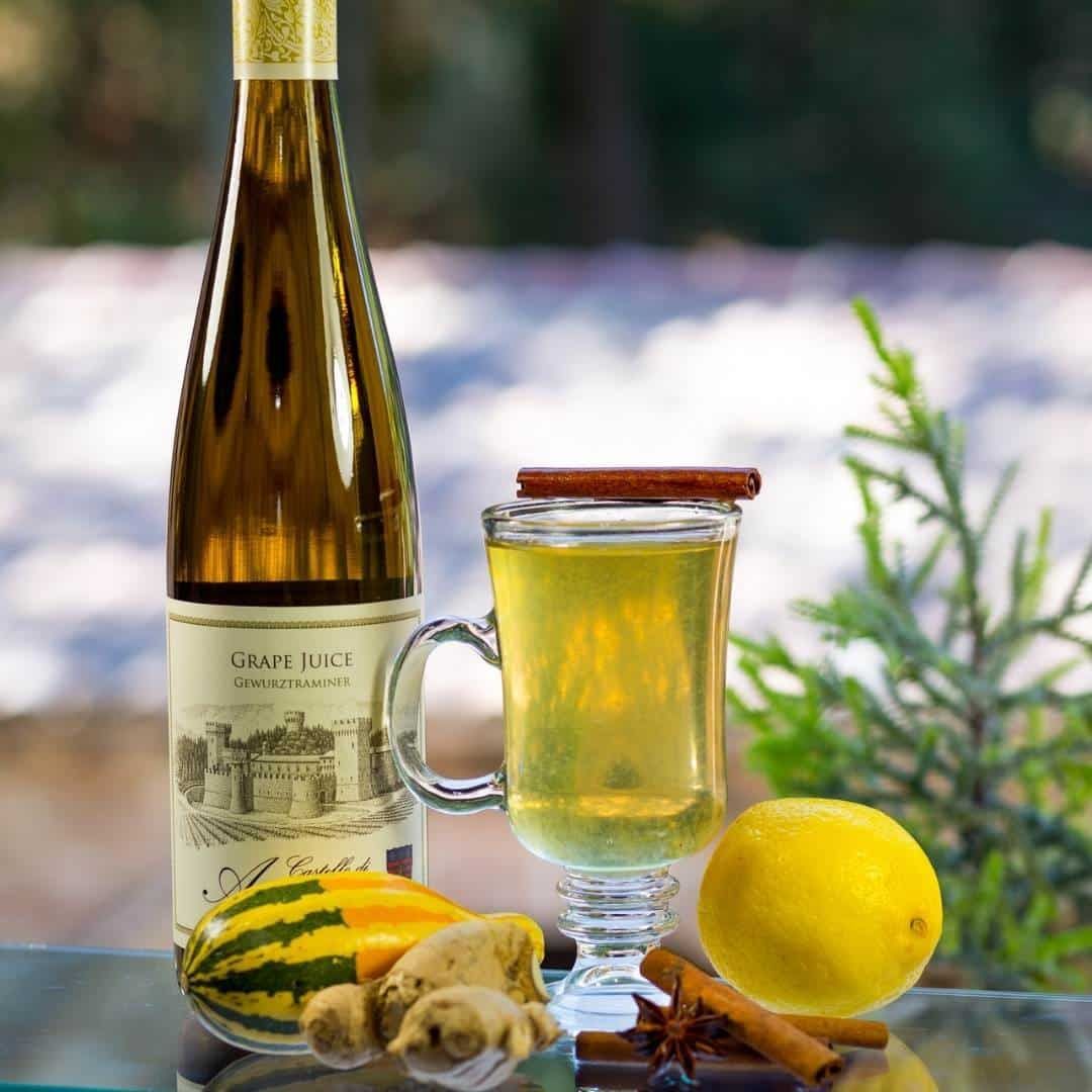 Bottle of white wine, a glass of hot toddy with cinnamon stick, lemon, ginger, and star anise.