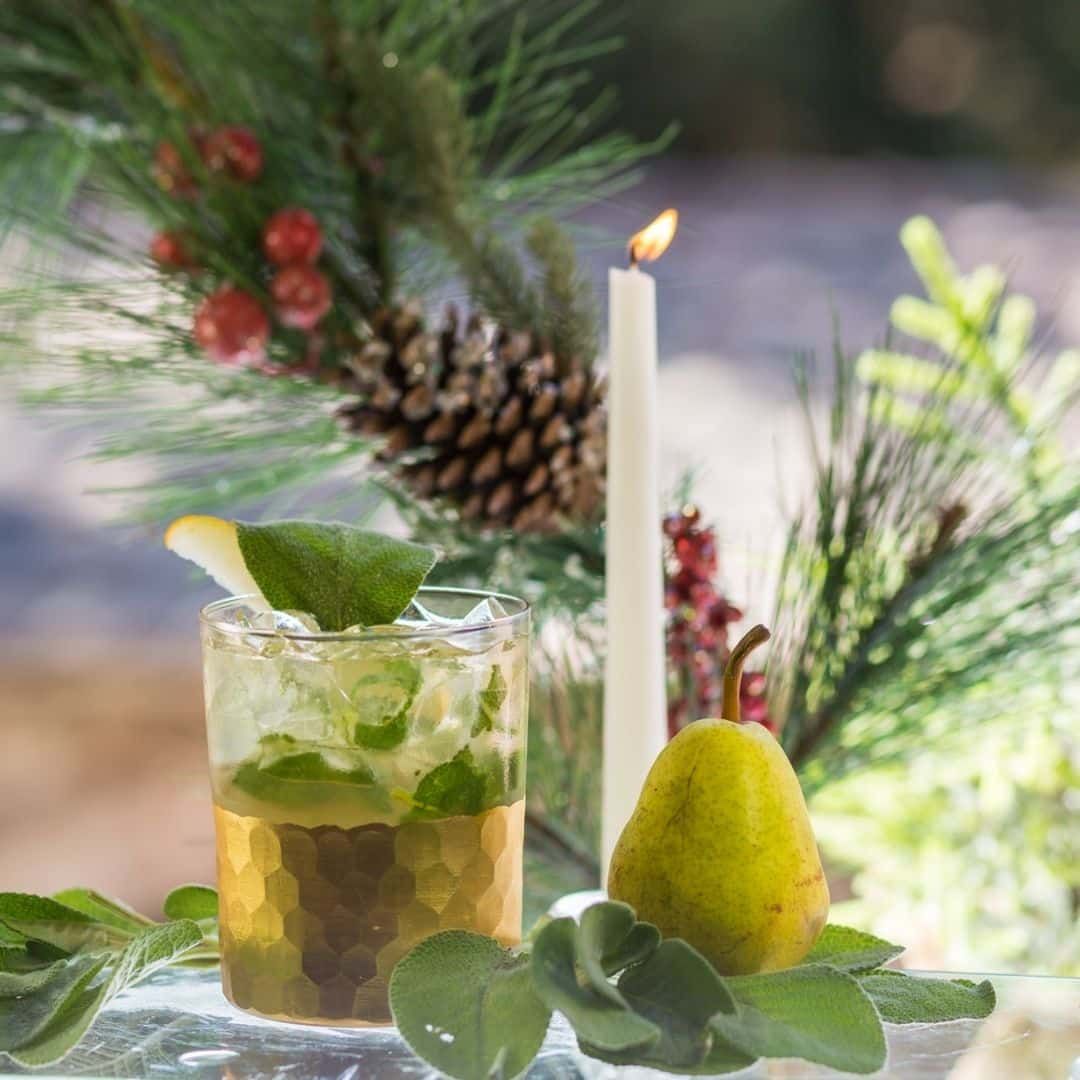 Cocktail with mint and ice, pear, candle, and pine branch.
