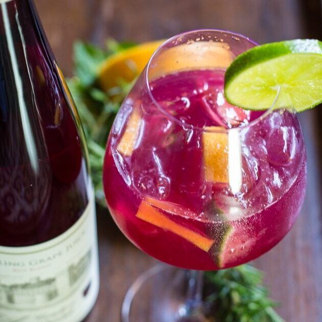 Sangria in a glass, with fruit slices and a lime wedge, next to a wine bottle.