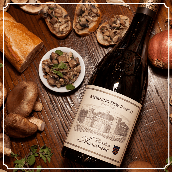 Bottle of Morning Dew Ranch wine with mushrooms, bread, and onions on a wooden table.