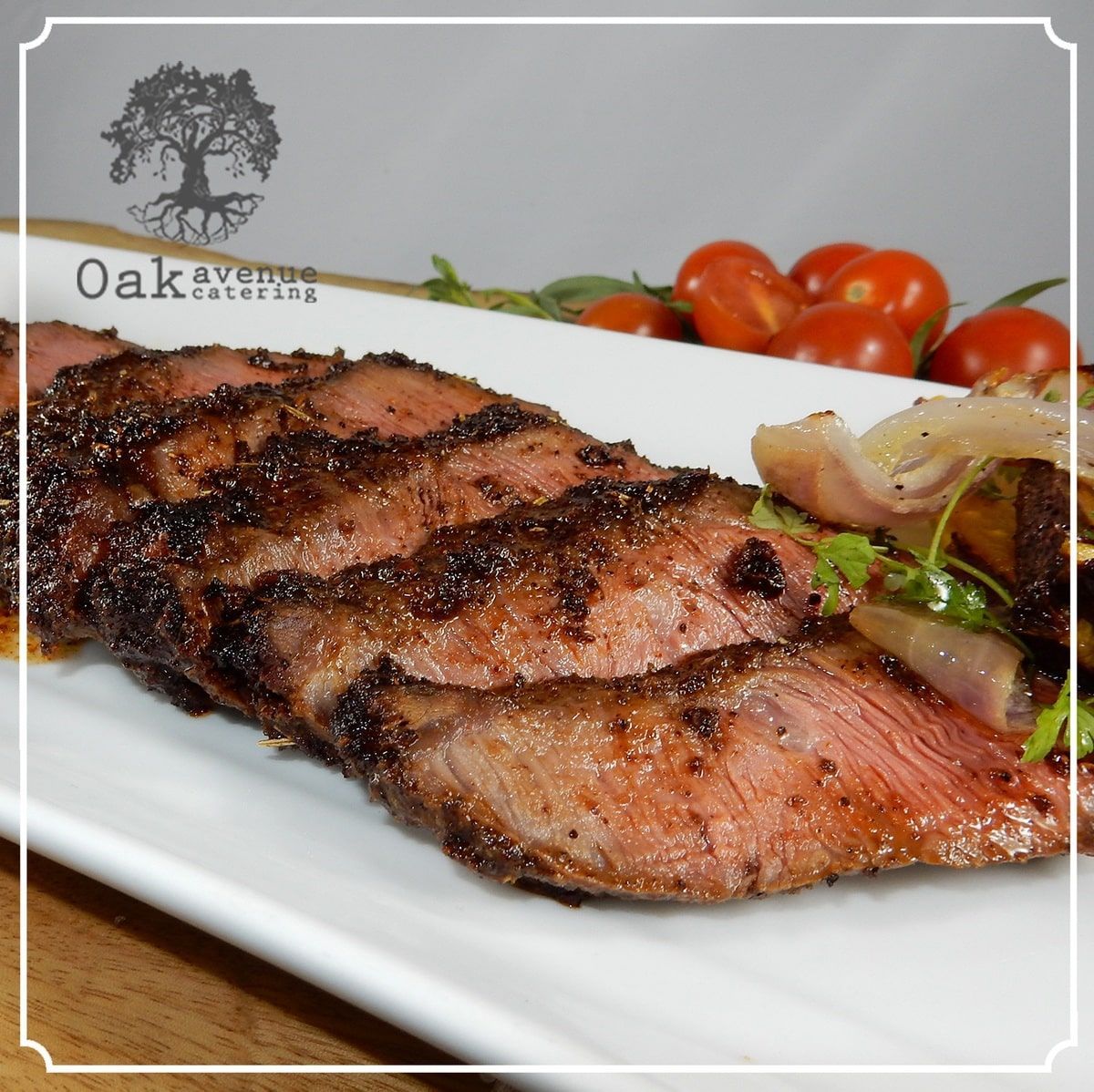 Sliced steak on a white plate with tomatoes and onions, catered by Oak Avenue.